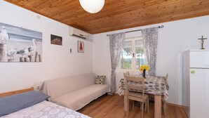 Una habitación acogedora con techo de madera, una cama con cubierta de encaje, un sofá, una mesa de comedor con sillas y un refrigerador.