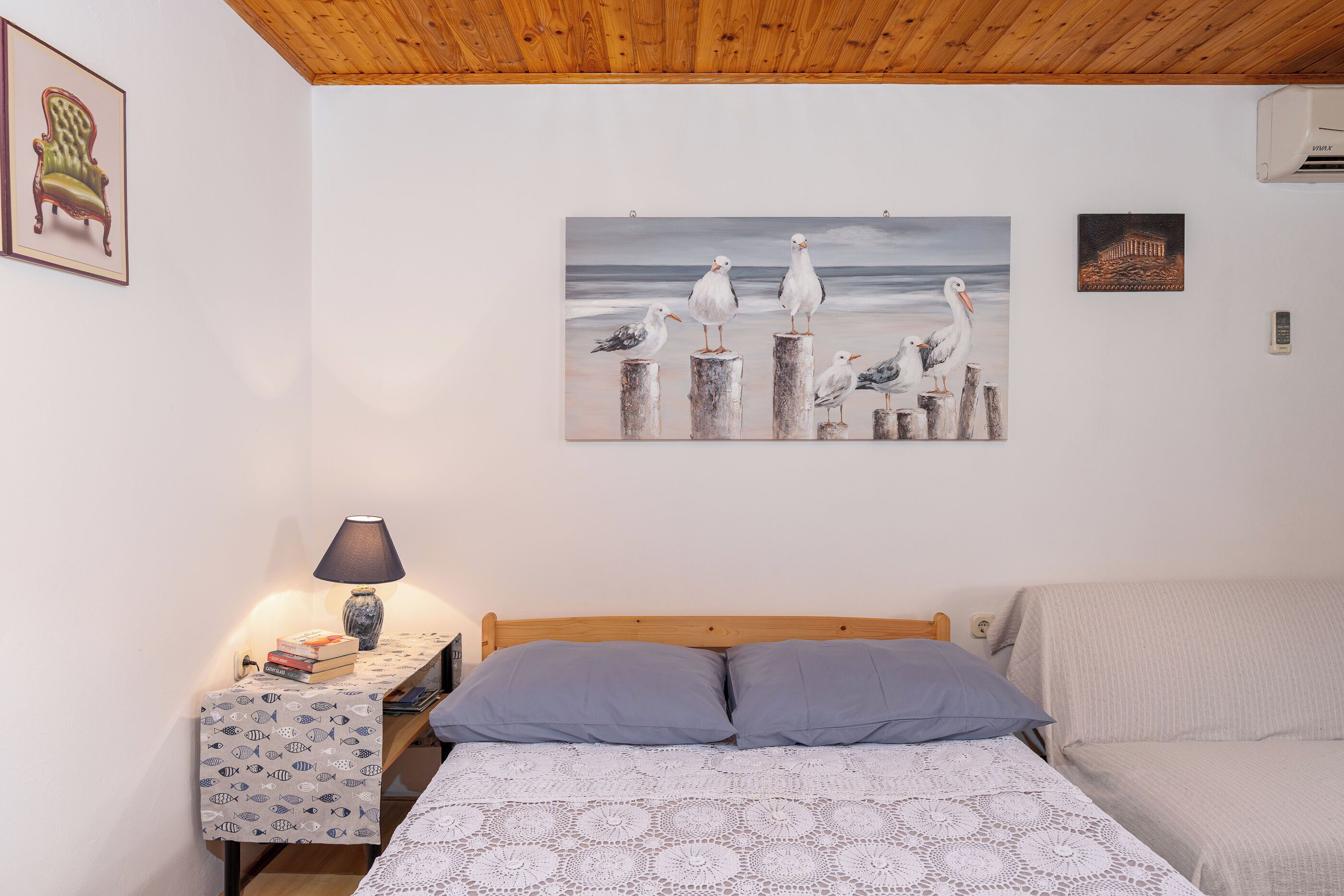 Ein Schlafzimmer mit Bett, Nachttisch, Lampe und einem Gemälde von Möwen an der Wand.