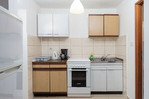 Cocina compacta con armarios blancos, encimera de madera, horno integrado y fregadero.