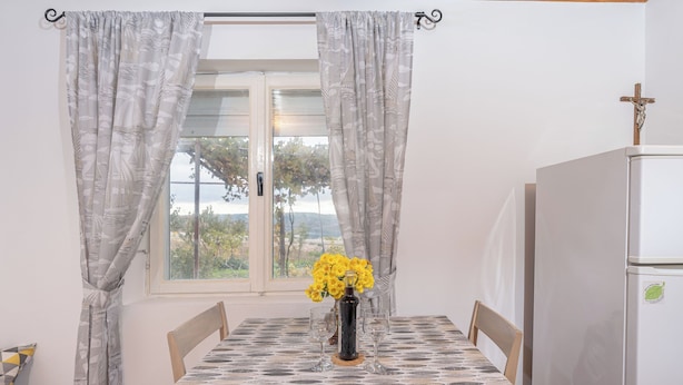 Una mesa de comedor con mantel estampado, un florero con flores amarillas y un refrigerador blanco con una cruz encima.