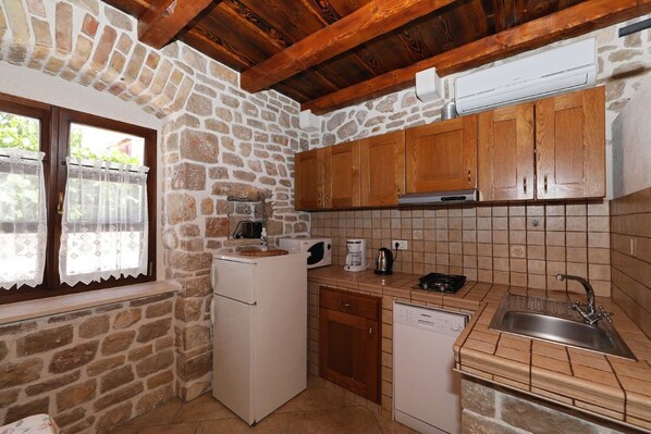 Una cocina compacta con paredes de piedra, armarios de madera, un refrigerador, lavavajillas y electrodomésticos básicos.