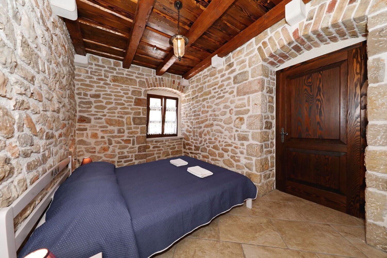 A room with a stone wall, a wooden door, and a bed with a blue bedspread.