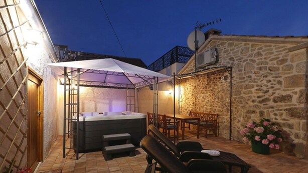 A hot tub with a canopy, outdoor seating, and a stone wall. - House Cirrus (Sukosan)