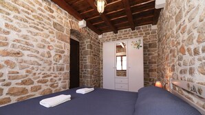 A bedroom with stone walls, a wooden ceiling, a bed with blue bedding, and a white wardrobe with a mirror. - House Cirrus (Sukosan)