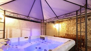 A hot tub under a tent with stone walls and a wooden table nearby. - House Cirrus (Sukosan)
