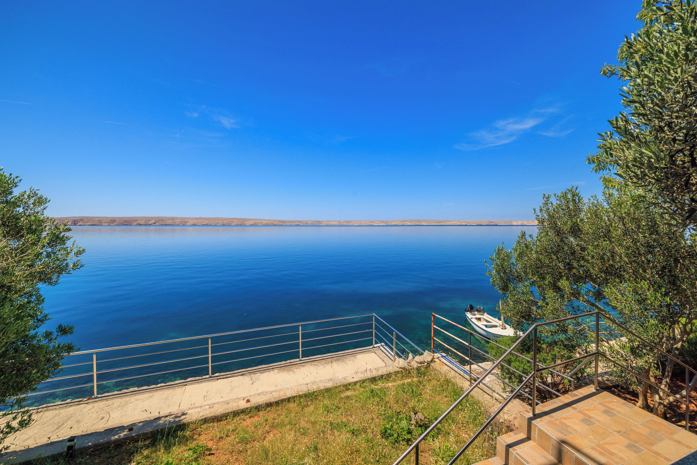 A coastal view with a clear sky, a boat docked near the shore, and a staircase leading down to the water.