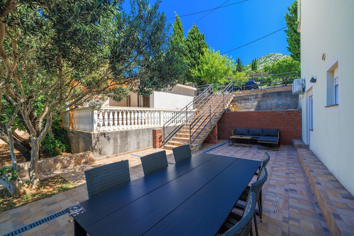 Eine Terrasse mit Tisch und Stühlen, eine Treppe und Blick auf einen Hügel.