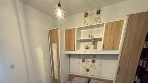 A bedroom with a bed, a hanging light fixture, built-in shelves, and a patterned wall. - Apartment Island of Love (Vir)