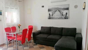 A living room with a black sofa, a glass table with red chairs, a checkered floor, a painting of a pier, and a window with curtains. - Apartment Island of Love (Vir)