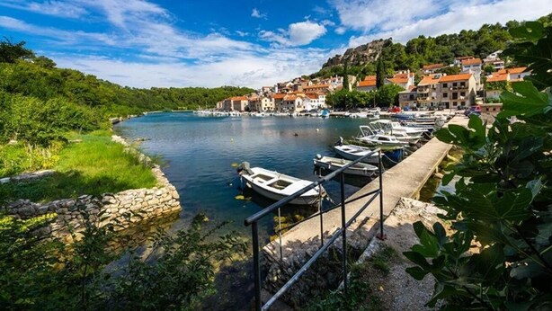 A riverside town with boats docked along the shore, a stone wall, and buildings with red roofs. - Apartment Mari (Novigrad)