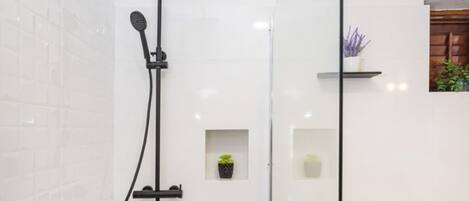 A modern shower area with a glass door, white tiled walls, and a wooden floor.