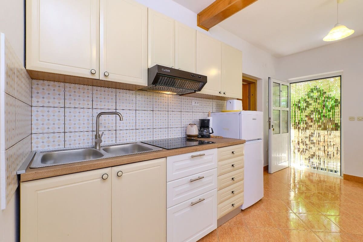 Una cocina con armarios blancos, un lavamanos de acero inoxidable, una cafetera y un refrigerador.