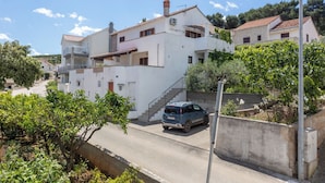 Un immeuble résidentiel à la façade blanche, avec un escalier menant à l’étage supérieur et une voiture garée dans l’allée.