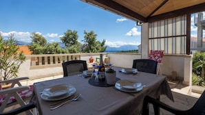 Un espace de restauration en plein air avec une table dressée pour deux personnes, une bouteille de vin et une plante en pot.