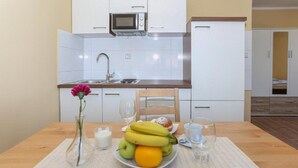 A small kitchenette with a microwave, sink, and cabinets. There is a dining table with fruits, a candle, and a vase with a flower. - Apartments Slavko With Terrace (Kastela)