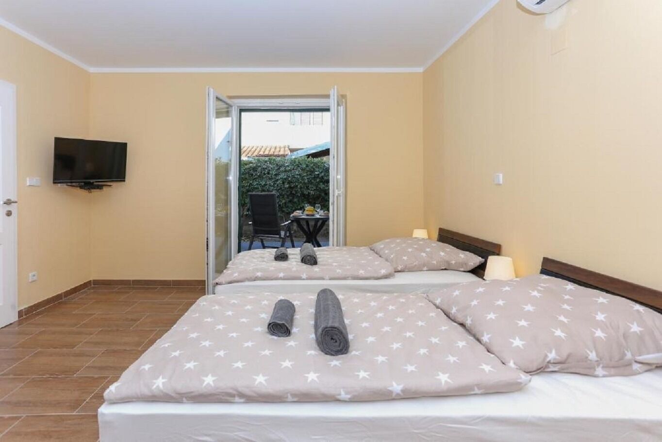 A hotel room with two beds, star-patterned bedding, a flat-screen TV, and a view of the outside.