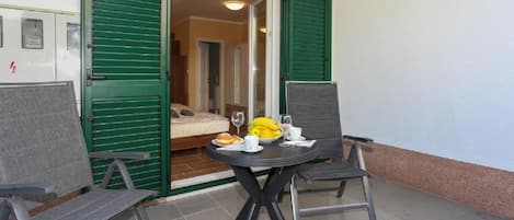 A small balcony with a table set for breakfast, including bread, bananas, and wine glasses.
