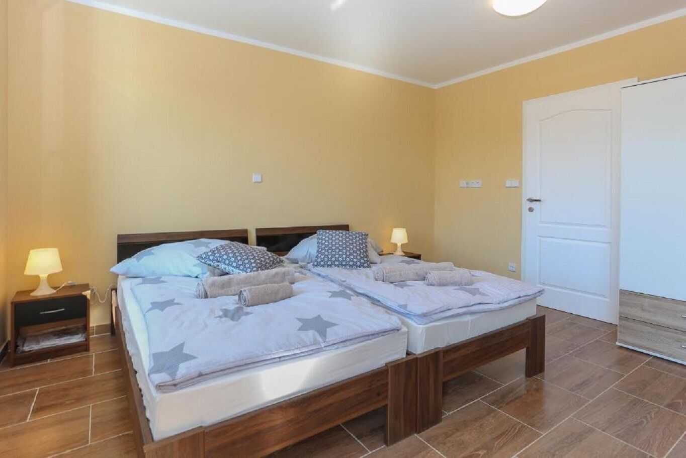 A double bed with a wooden frame, two bedside tables with lamps, and a white door.