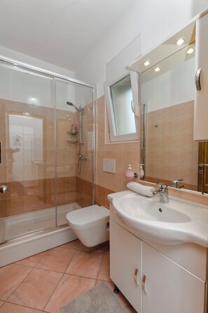 A bathroom with a glass-enclosed shower, a white sink, and a mirror above the sink. - Apartment Denko by the sea (Tisno)