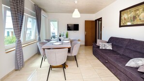 A dining area with a table set for four, a sofa, a TV mounted on the wall, and a door leading to another room. - Apartment Denko by the sea (Tisno)