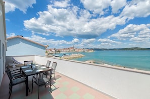 A balcony with a table set for dining, overlooking a coastal town with clear skies and a calm sea. - Apartment Denko by the sea (Tisno)