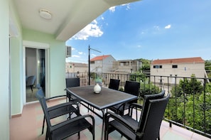 A balcony with a table and chairs, a potted plant, and a view of neighboring buildings. - Apartment Denko by the sea (Tisno)