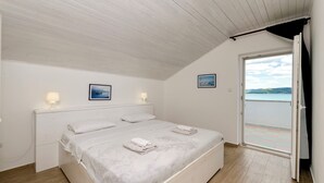 A bedroom with a bed, two bedside lamps, a window with a view, and a door leading to an outdoor balcony. - Apartment Denko by the sea (Tisno)