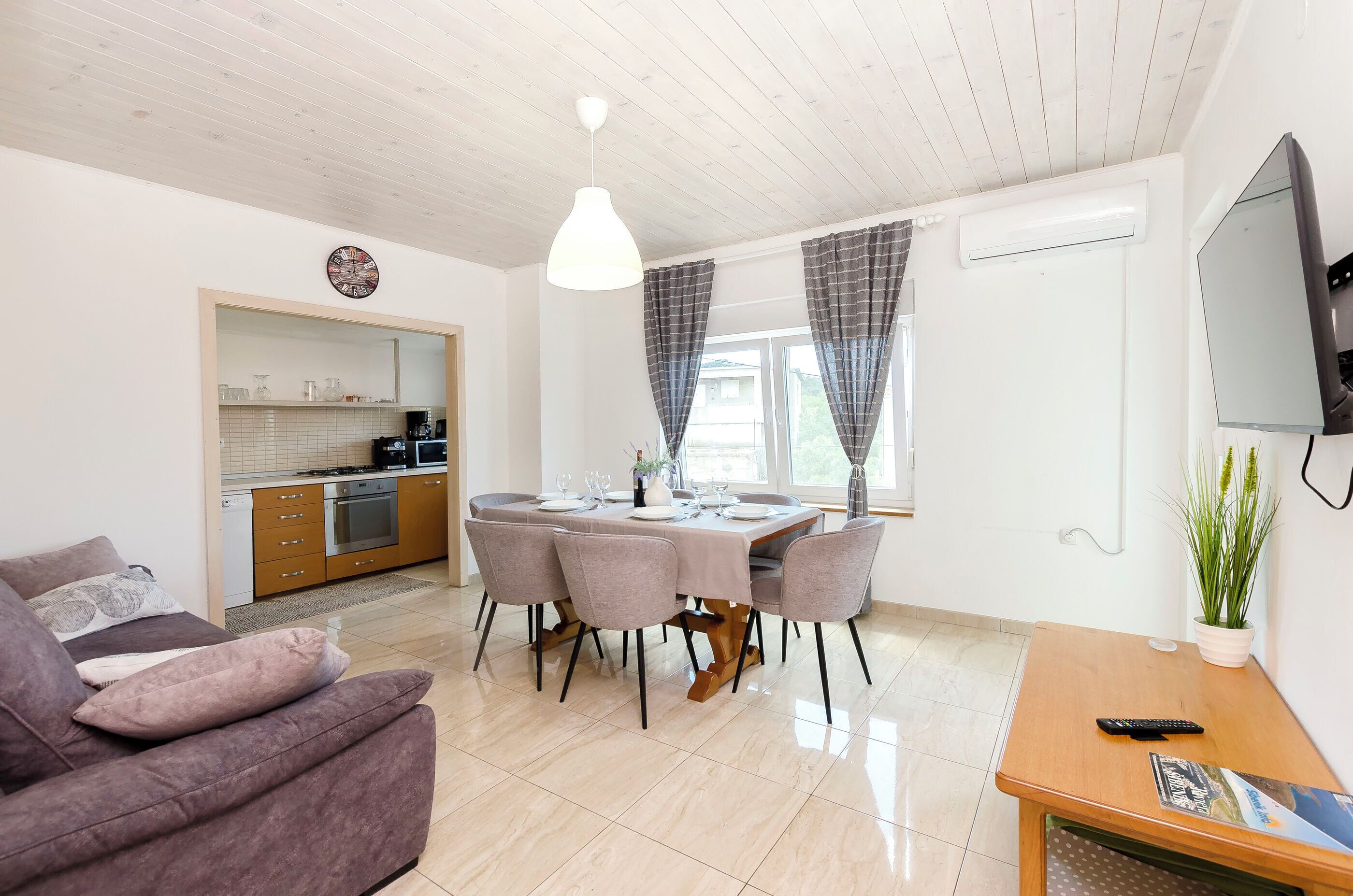 A modern living room with a dining table, sofa, TV, and kitchen in the background.