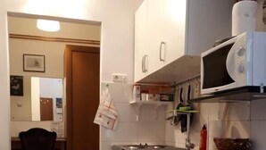 A compact kitchen with white cabinets, a microwave, and a small sink. There is a chair in the adjacent room and a striped rug on the floor. - Apartment Milan (Zagreb)