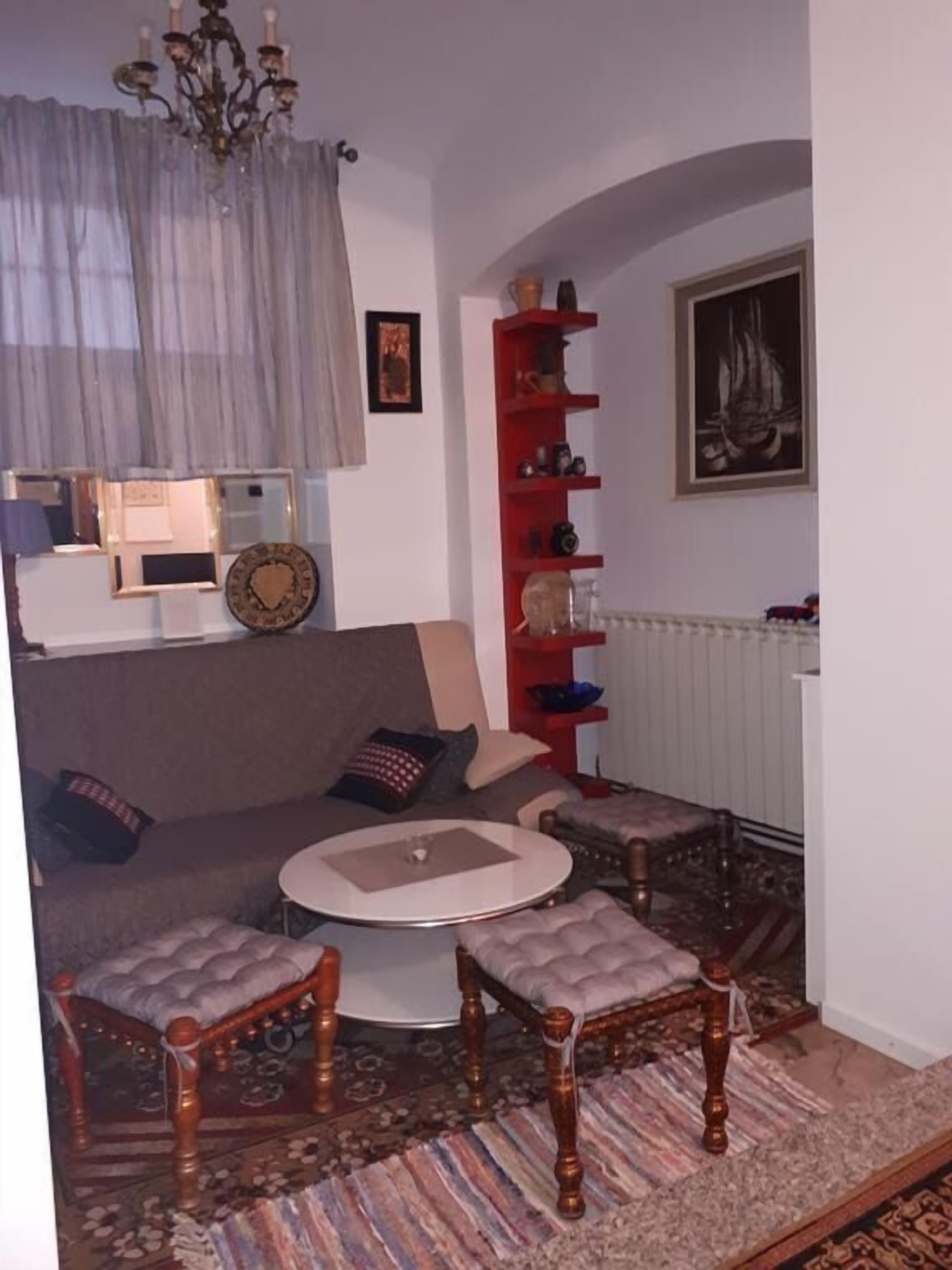 Una sala de estar acogedora con un sofá, dos sillones, una mesita de centro, una estantería roja, un candelabro y un cuadro enmarcado en la pared.