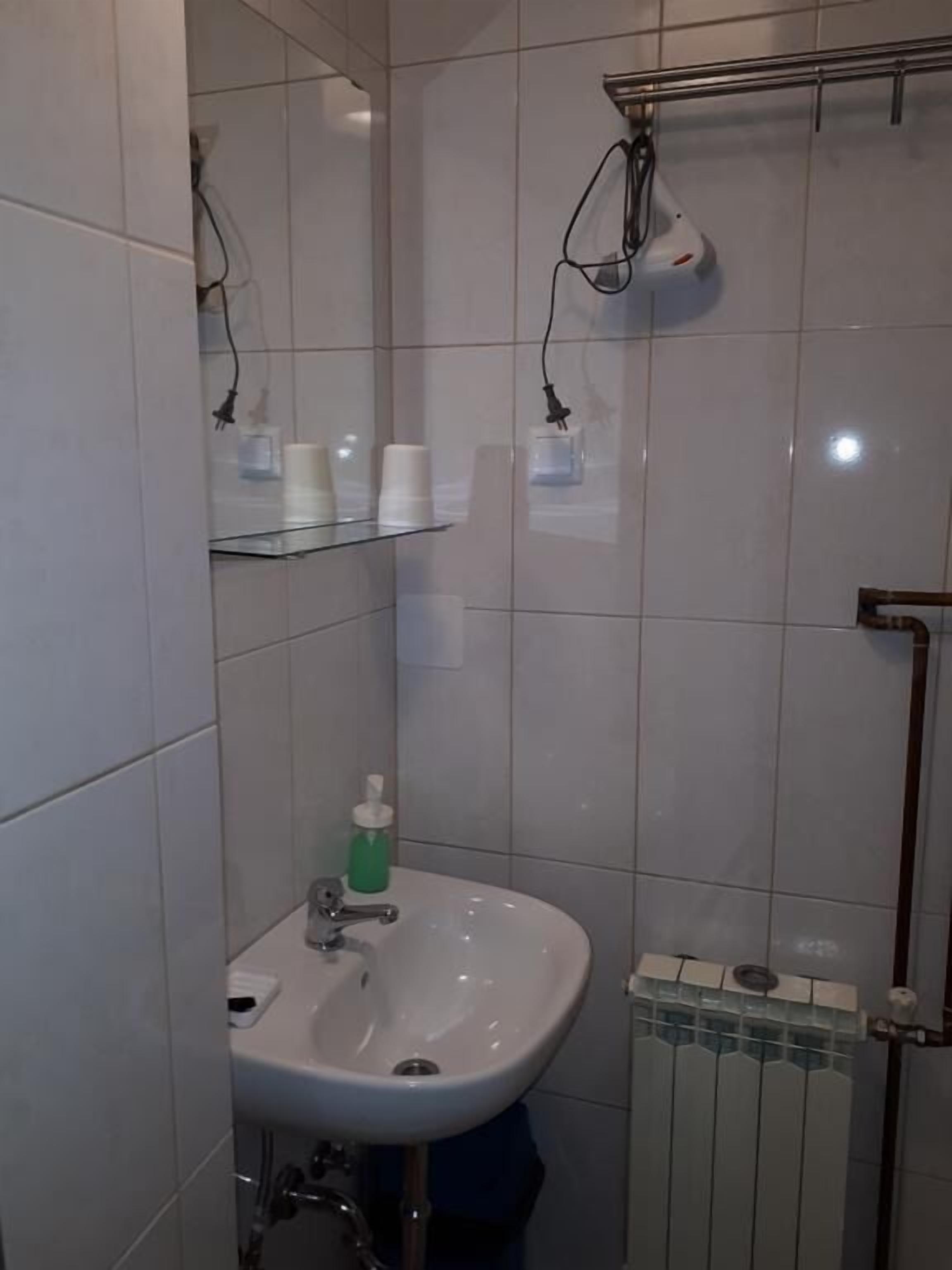 Een badkamer met een wit wastafelmeubel, een spiegel en een handdoekhouder. Boven de wastafel staan planken met toiletartikelen.
