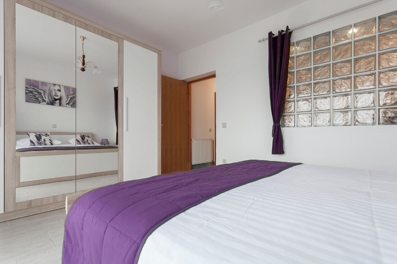 Ein Schlafzimmer mit Bett, Kleiderschrank, Spiegel und einem Fenster mit Vorhängen.