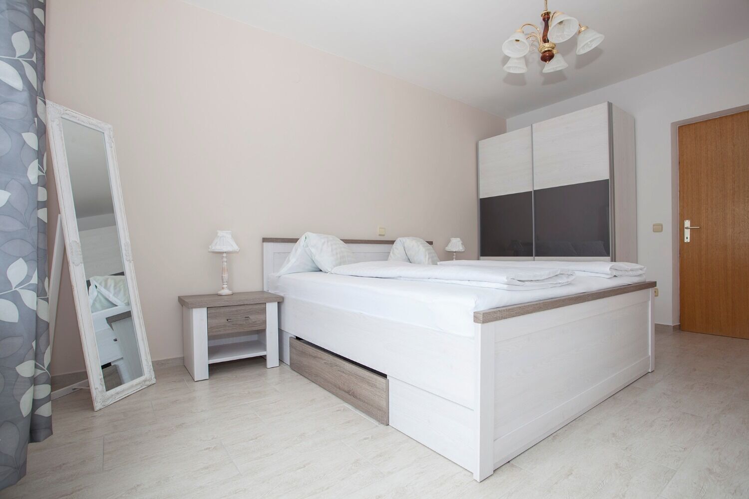 A modern bedroom with a bed, nightstands, a mirror, and a wardrobe.