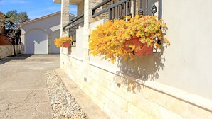 Un edificio con paredes de piedra y una puerta de garaje. Hay macetas con flores en la pared y un camino de grava en el frente.
