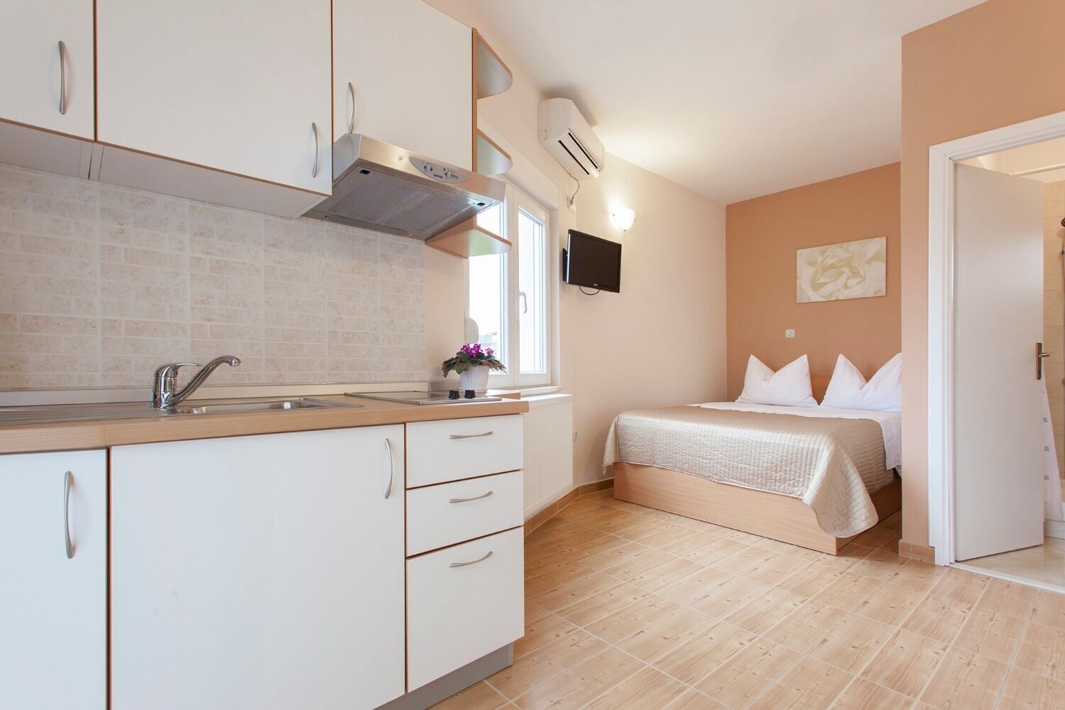 Une chambre d’hôtel compacte dotée d’une kitchenette, d’un lit avec une literie blanche et d’un téléviseur à écran plat fixé au mur.