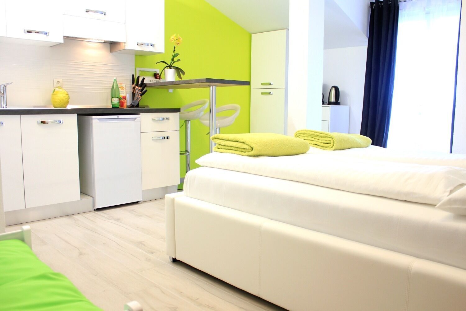 Ein kompaktes Hotelzimmer mit Bett, einer kleinen Küchenzeile und einer Wand in Grünton.