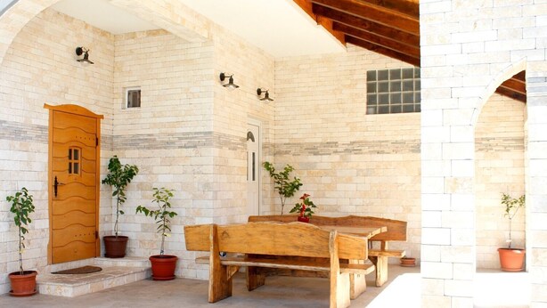 Un patio exterior con una mesa de madera y bancos, rodeado de muros de piedra y plantas en macetas.
