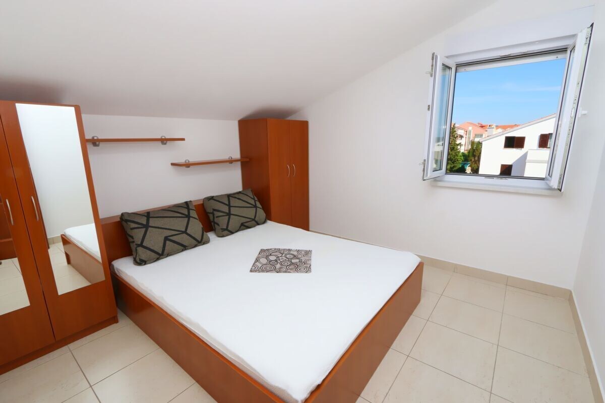 Ein Schlafzimmer mit Bett, Kleiderschrank, Fenster und Blick auf Gebäude.