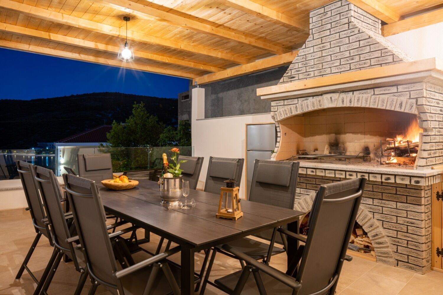 An outdoor dining area with a brick fireplace, a table set for two, and a view of the mountains in the background.