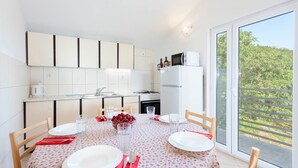 A compact kitchen with white cabinets, a refrigerator, and a dining area with a table set for two. - House Tonci (Tucepi)