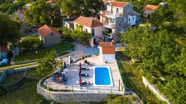 An aerial view of a residential area with a swimming pool, stone walls, and houses with red-tiled roofs. - House Tonci (Tucepi)