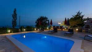 A swimming pool with lounge chairs and umbrellas, surrounded by a stone deck and a stone wall. - House Tonci (Tucepi)