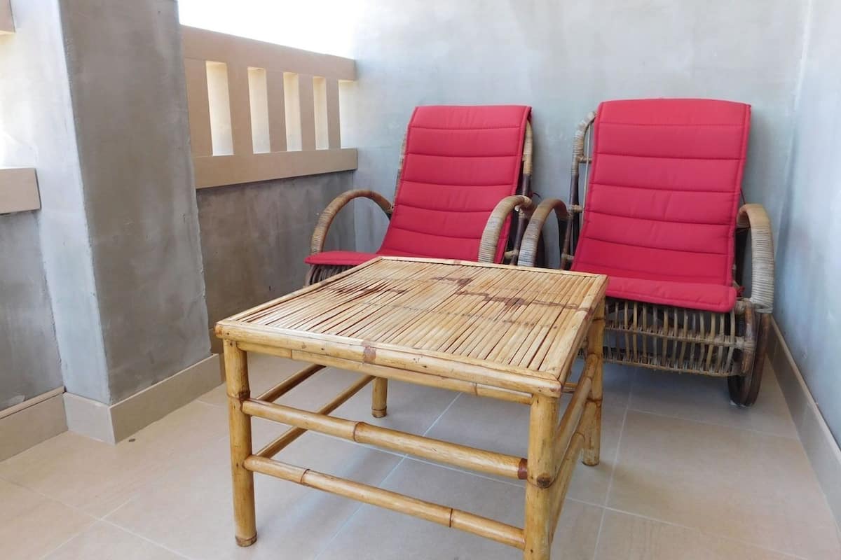 A bamboo table and two wicker chairs with red cushions in a room with tiled flooring and a light-colored wall.