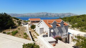 Ein Küstenhaus mit Ziegeldach, einem sichtbaren Uhrwerk und Blick auf Meer und Berge im Hintergrund.