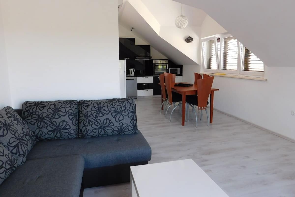 A modern living space with a sofa, dining table, and chairs. A kitchen is visible in the background.