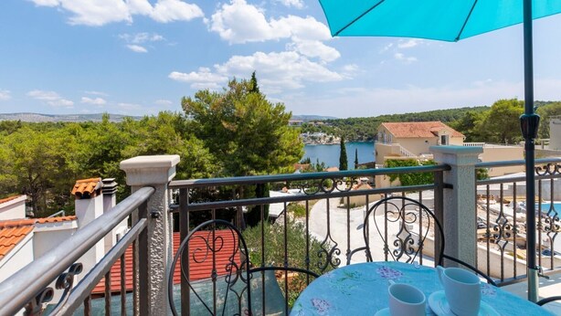 A balcony with a view of a lake, trees, and buildings. - Apartments Dalis (Milna)