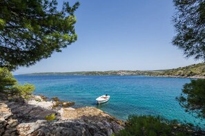 A coastal scene with a boat on calm blue waters, rocky shore, and clear skies. - Apartments Dalis (Milna)