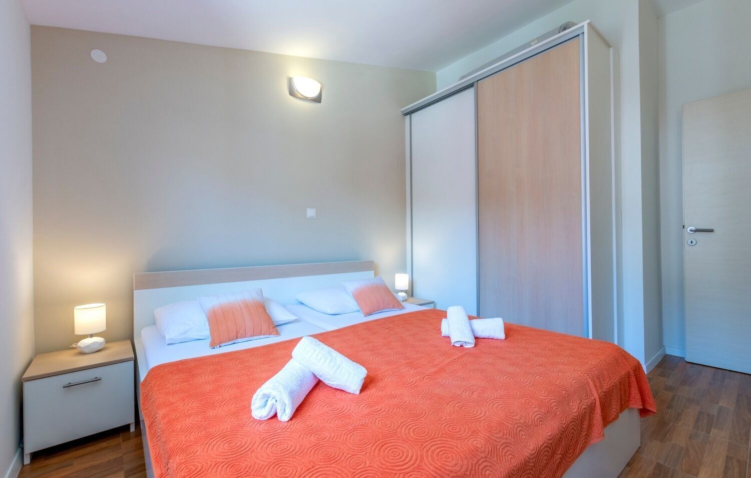 A hotel room with a bed, nightstands, a wardrobe, and a door.