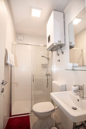 A modern bathroom with a glass shower enclosure, a white toilet, and a sink with a mirror above it. - Apartments Andelko (Baska Voda)