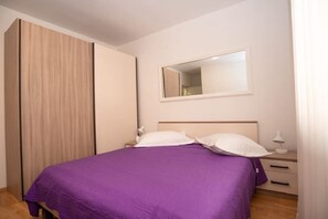 A bedroom with a bed, a nightstand, a mirror, and a wardrobe. - Apartments Andelko (Baska Voda)